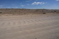 an empty dirt road in the middle of a desert area with a white and black fire hydrant near it