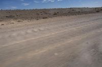 an empty dirt road in the middle of a desert area with a white and black fire hydrant near it