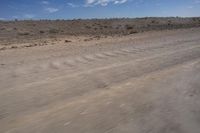 an empty dirt road in the middle of a desert area with a white and black fire hydrant near it