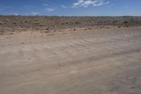 an empty dirt road in the middle of a desert area with a white and black fire hydrant near it