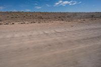 an empty dirt road in the middle of a desert area with a white and black fire hydrant near it