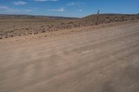 an empty dirt road in the middle of a desert area with a white and black fire hydrant near it