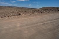 an empty dirt road in the middle of a desert area with a white and black fire hydrant near it