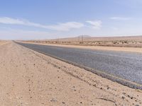 empty road near desert area with mountains in background, no people yet on it, in the distance are bushes and sparse clouds