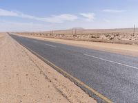 empty road near desert area with mountains in background, no people yet on it, in the distance are bushes and sparse clouds