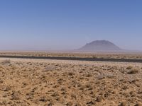 the desert in the middle of nowhere with the mountain in the distance behind it near a paved road