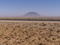 the desert in the middle of nowhere with the mountain in the distance behind it near a paved road