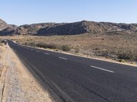 an empty highway on the road next to mountains and sand areas with trees in the background