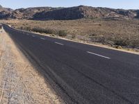 an empty highway on the road next to mountains and sand areas with trees in the background