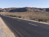 an empty highway on the road next to mountains and sand areas with trees in the background