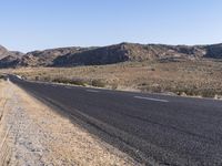 an empty highway on the road next to mountains and sand areas with trees in the background