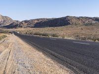 an empty highway on the road next to mountains and sand areas with trees in the background