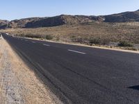 an empty highway on the road next to mountains and sand areas with trees in the background