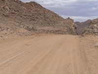 a small vehicle traveling across a barren road between some large rocks and boulders on one side