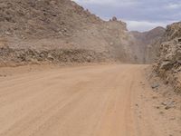 a small vehicle traveling across a barren road between some large rocks and boulders on one side