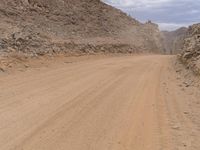 a small vehicle traveling across a barren road between some large rocks and boulders on one side