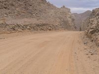 a small vehicle traveling across a barren road between some large rocks and boulders on one side