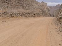 a small vehicle traveling across a barren road between some large rocks and boulders on one side