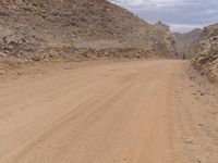 a small vehicle traveling across a barren road between some large rocks and boulders on one side