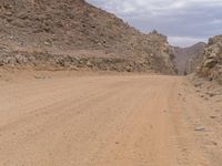 a small vehicle traveling across a barren road between some large rocks and boulders on one side