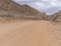 a small vehicle traveling across a barren road between some large rocks and boulders on one side