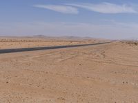 empty road near desert area with mountains in background, no people yet on it, in the distance are bushes and sparse clouds