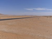 empty road near desert area with mountains in background, no people yet on it, in the distance are bushes and sparse clouds