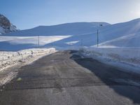 a road in the mountains in the sun covered by snow with a snow plow on it