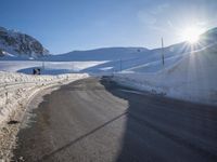 a road in the mountains in the sun covered by snow with a snow plow on it