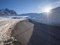 a road in the mountains in the sun covered by snow with a snow plow on it