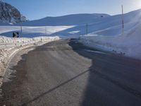 a road in the mountains in the sun covered by snow with a snow plow on it