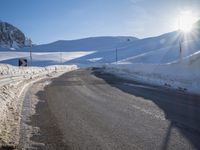 a road in the mountains in the sun covered by snow with a snow plow on it