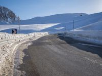 a road in the mountains in the sun covered by snow with a snow plow on it