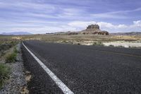 a lone road in an arid landscape with mountains in the distance and a sky above it