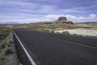 a lone road in an arid landscape with mountains in the distance and a sky above it