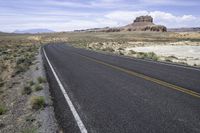 a lone road in an arid landscape with mountains in the distance and a sky above it