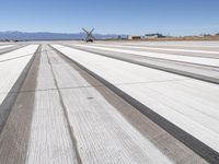 a runway with mountains in the background, snow on the ground and a small plane parked in the distance