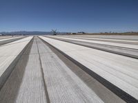 a runway with mountains in the background, snow on the ground and a small plane parked in the distance