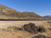 a road leads through the middle of desert land next to mountains and dirt road leading into the distance