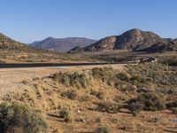 a road leads through the middle of desert land next to mountains and dirt road leading into the distance