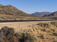 a road leads through the middle of desert land next to mountains and dirt road leading into the distance