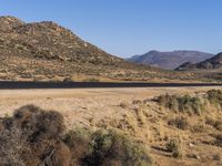 a road leads through the middle of desert land next to mountains and dirt road leading into the distance