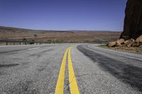 an empty desert road stretches in the distance with mountains in the background and yellow lines painted on both sides