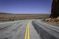 an empty desert road stretches in the distance with mountains in the background and yellow lines painted on both sides