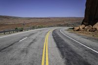 an empty desert road stretches in the distance with mountains in the background and yellow lines painted on both sides