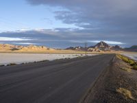 an empty desert road in the middle of nowhere in front of a hill covered with sand and dry grass