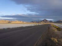 an empty desert road in the middle of nowhere in front of a hill covered with sand and dry grass