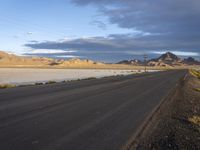 an empty desert road in the middle of nowhere in front of a hill covered with sand and dry grass