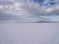 a large expanse full of snow in the desert with mountains in the background under cloudy skies