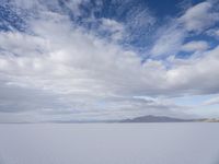 a large expanse full of snow in the desert with mountains in the background under cloudy skies